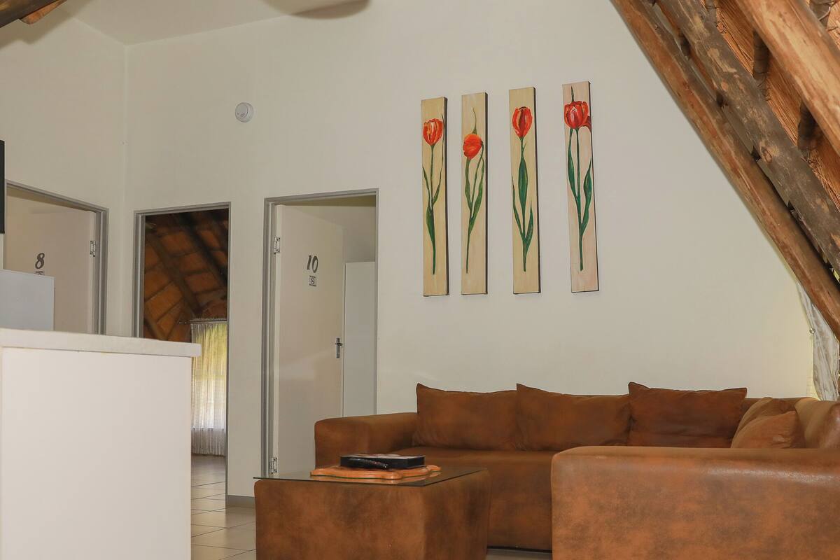 A living room with a brown sectional sofa, a small table, and a white cabinet. There are four paintings of red tulips on the wall.