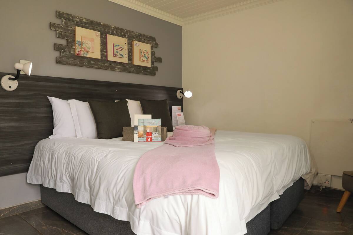 A hotel room with a large bed, a headboard, a bedside table, a lamp, and a wall-mounted artwork.