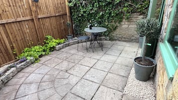 A patio with stone tiles, a wooden fence, a table with chairs, and potted plants.