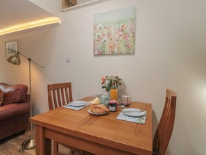 A dining table with chairs, a vase with flowers, a bottle of juice, a plate with croissants, and a cup. - Wheelwright Cottage (Moreton-in-Marsh)