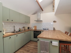 A kitchen with light green cabinets, a wooden countertop, a built-in oven, and a tiled backsplash. - Wheelwright Cottage (Moreton-in-Marsh)