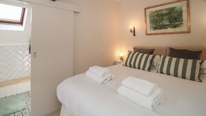 Quarto com cama, almofadas, mesa de cabeceira, luminária na parede e um quadro emoldurado.