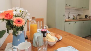 Uma cozinha com mesa de madeira posta para o café da manhã, incluindo um vaso com flores, um jarro de suco de laranja e um prato com croissants.