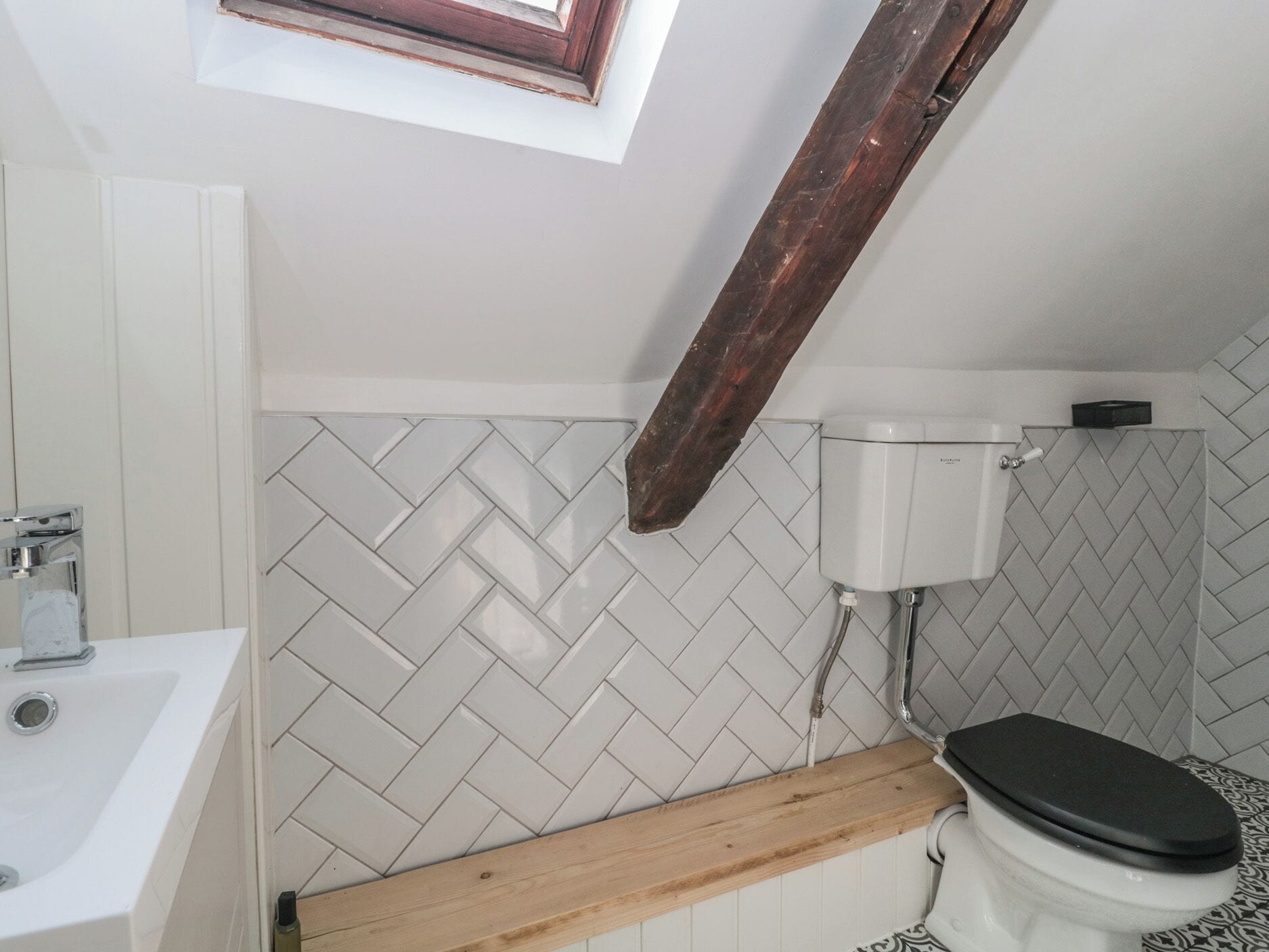 A bathroom with a white herringbone tile backsplash, a white toilet, a wooden vanity, and a skylight.