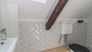 A bathroom with a white herringbone tile backsplash, a white toilet, a wooden vanity, and a skylight.