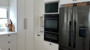 Une cuisine moderne avec des meubles blancs, un réfrigérateur en acier inoxydable et un four encastré.
