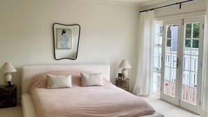 Une chambre avec un grand lit, deux tables de chevet, un tableau accroché au mur et une vue sur l’extérieur, visible à travers une porte vitrée.
