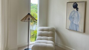 Une pièce dotée d’une grande fenêtre, d’un lampadaire, d’un fauteuil confortable et d’une œuvre d’art encadrée accrochée au mur.