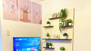 A living room with a TV, shelves with plants, a calendar, and artwork on the wall.