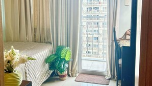 A hotel room with a bed, a potted plant, a desk, and a view of a building through a window.