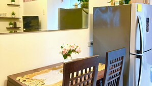 A dining area with a table, chairs, a refrigerator, and a mirror.