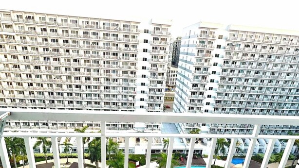 A high-rise building with multiple balconies, a pool area with clear blue water, and a view of the surrounding buildings.