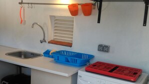 Pieni, käytännöllinen keittiö, jossa on pesuallas, pyykinpesukone, sininen muovikori ja oranssit säilytysastiat seinällä.