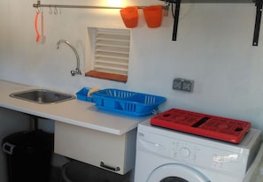 Eine kleine Küche mit Spüle, Waschmaschine, einem blauen Plastikkorb und orangenen Behältern an der Wand.