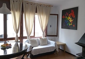 Ein Zimmer mit einem Bett, einem Tisch mit Obst, einem kleinen Tisch, einer Lampe und einem Gemälde an der Wand.