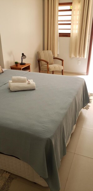 A neatly made bed with a blue bedspread and white towels, a wooden chair, a small table with a lamp, and a window with curtains. - Vila de Cunha Inn (Cunha)