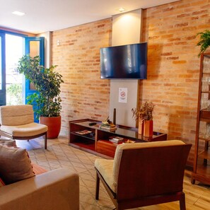 A modern living room with a brick wall, a flat-screen TV mounted above a wooden coffee table, and comfortable seating. - Vila de Cunha Inn (Cunha)