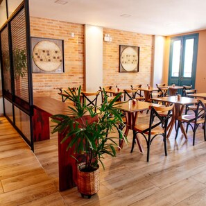 A restaurant with brick walls, wooden tables, and chairs. There are potted plants and framed artwork on the walls. - Vila de Cunha Inn (Cunha)