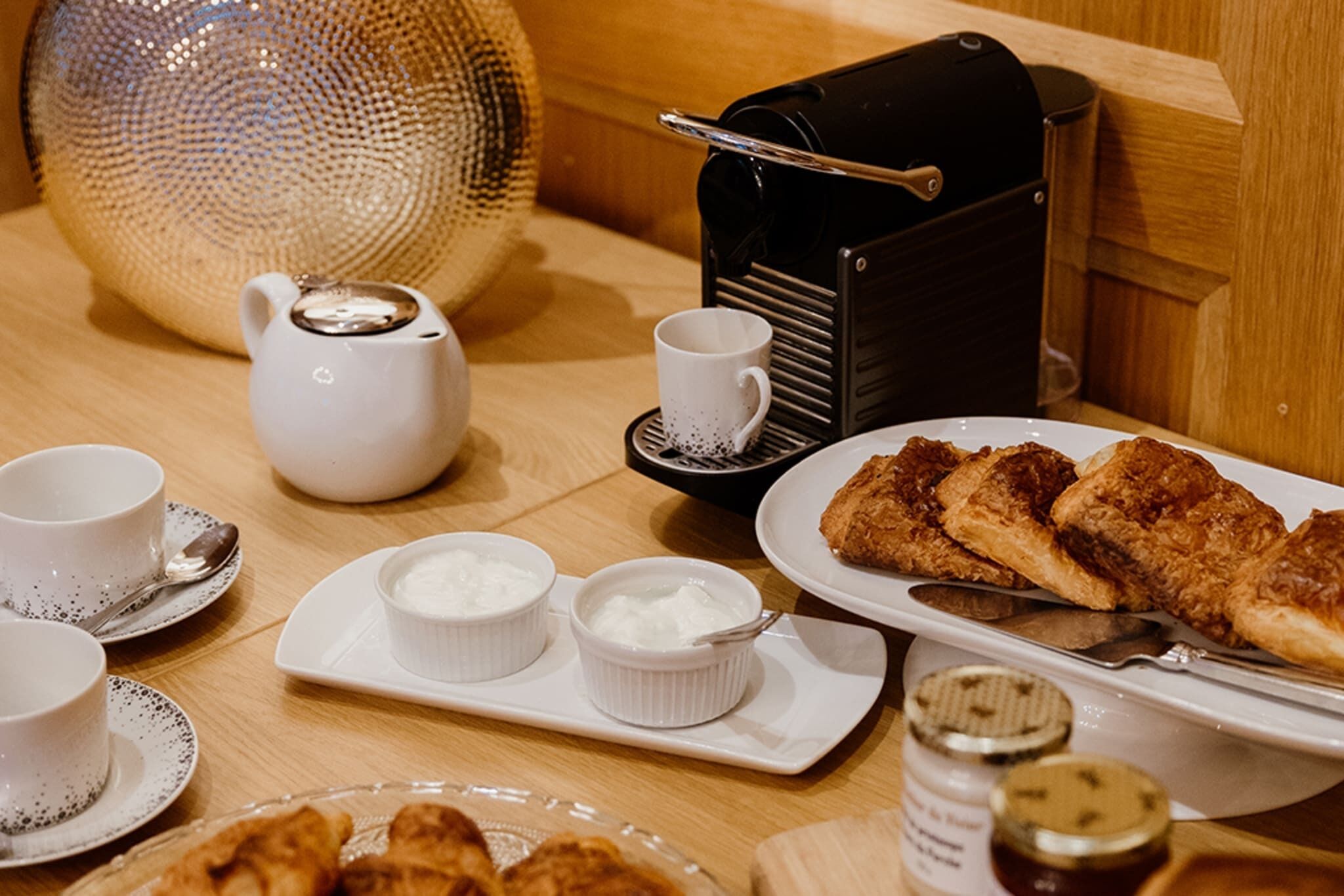 A breakfast setting with a teapot, cups, a plate of fried food, and condiments.