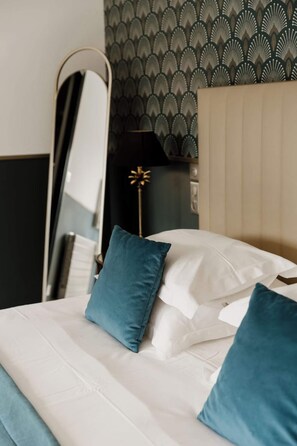 Ein ordentlich gemachtes Bett mit weißen und türkisblauen Kissen, ein Spiegel und eine Wand mit Muster.