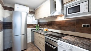 A modern kitchen with stainless steel appliances, wooden cabinets, and a granite countertop. - DALI Apartment - Right in the city centre (Salou)