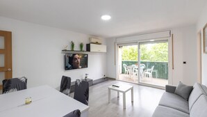 A modern living room with a flat-screen TV, a sofa, a dining table, and a sliding glass door leading to an outdoor area. - DALI Apartment - Right in the city centre (Salou)