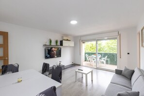 Una sala de estar moderna con una televisión de pantalla plana, un sofá, una mesa de comedor y un gran ventanal corredizo que da a un espacio exterior.