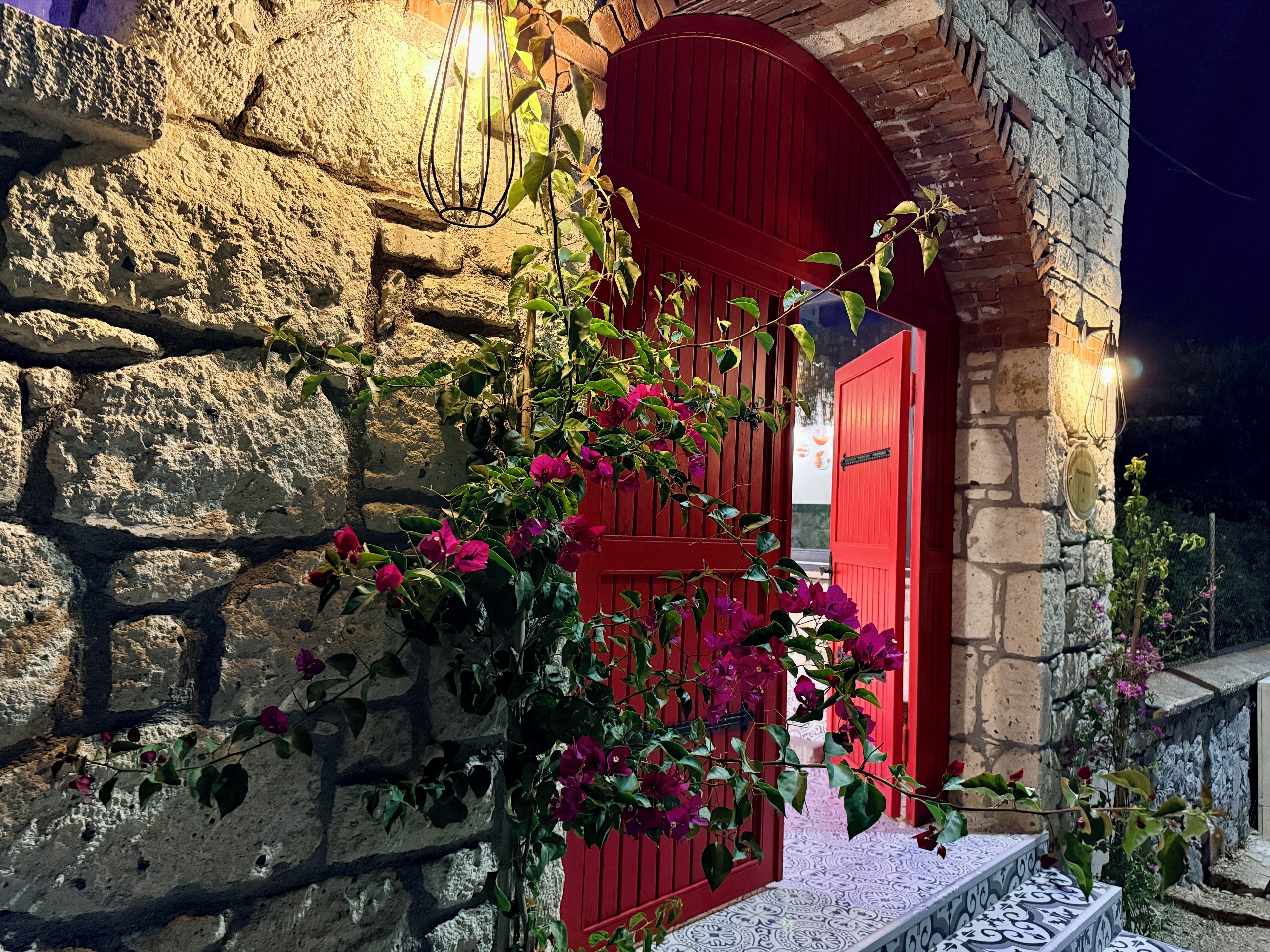 Un bâtiment en pierre avec une porte rouge et un escalier menant à l’entrée.