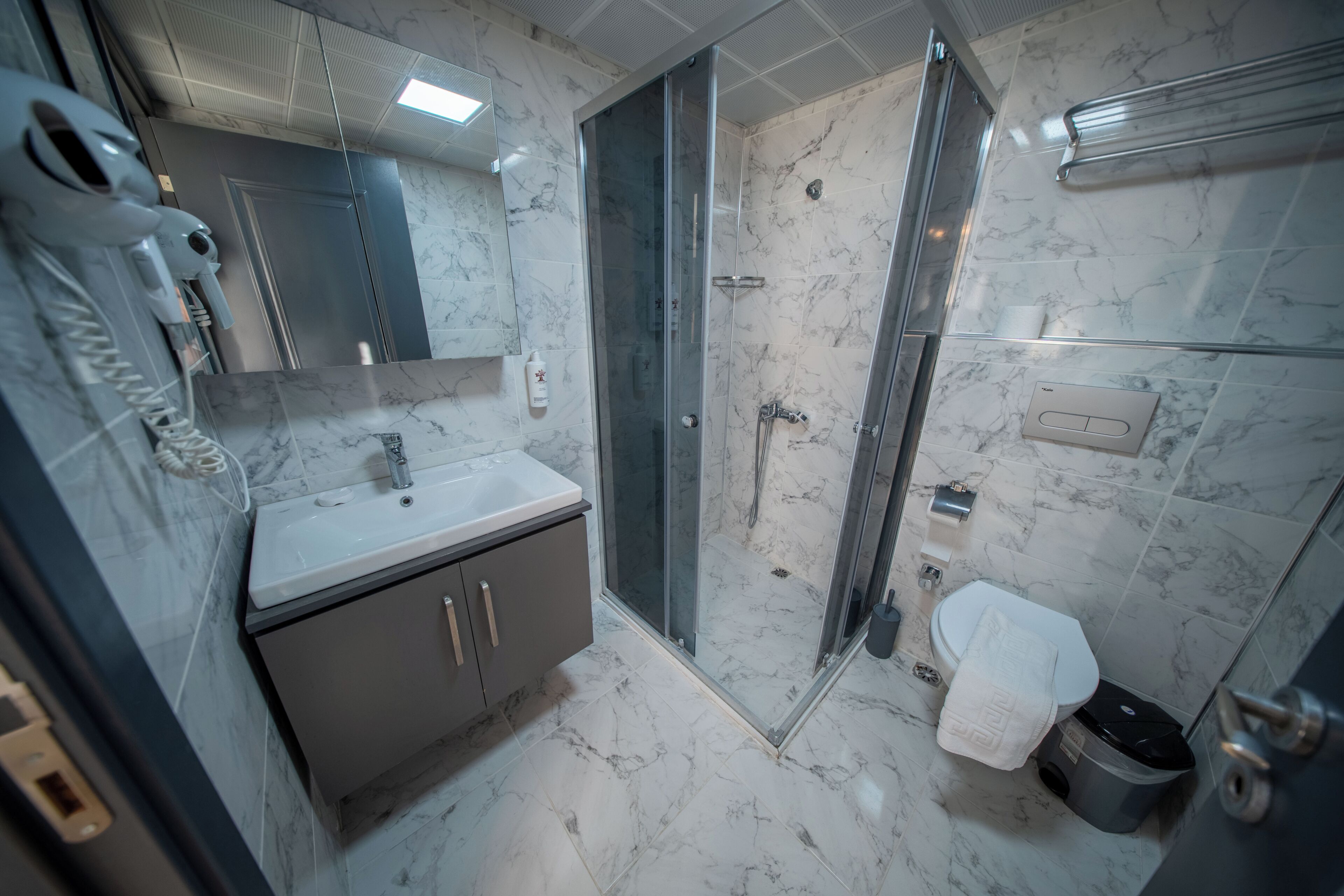 Un baño con suelo de mármol, lavabo, espejo, ducha con mampara de cristal y toallero.