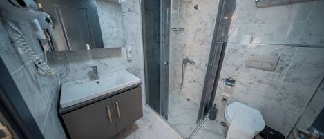 Un baño con suelo de mármol, lavabo, espejo, ducha con mampara de cristal y toallero.