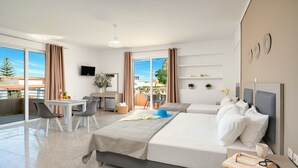 Ein Hotelzimmer mit Balkon, Schreibtisch mit Stuhl, zwei Betten, Fernseher und ein kleiner Tisch mit Vase und Blumen.