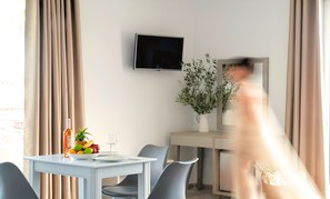 A hotel room with a dining table, chairs, a television on the wall, and a potted plant.