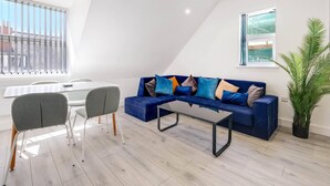 Ein modernes Wohnzimmer mit einem blauen Sofa, grauen Sesseln, einem Glastisch und einem Topf mit Pflanze.