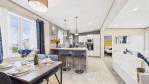 Een moderne keuken met barstoelen, een eettafel voor twee personen en een zithoek met een bank en een bed.