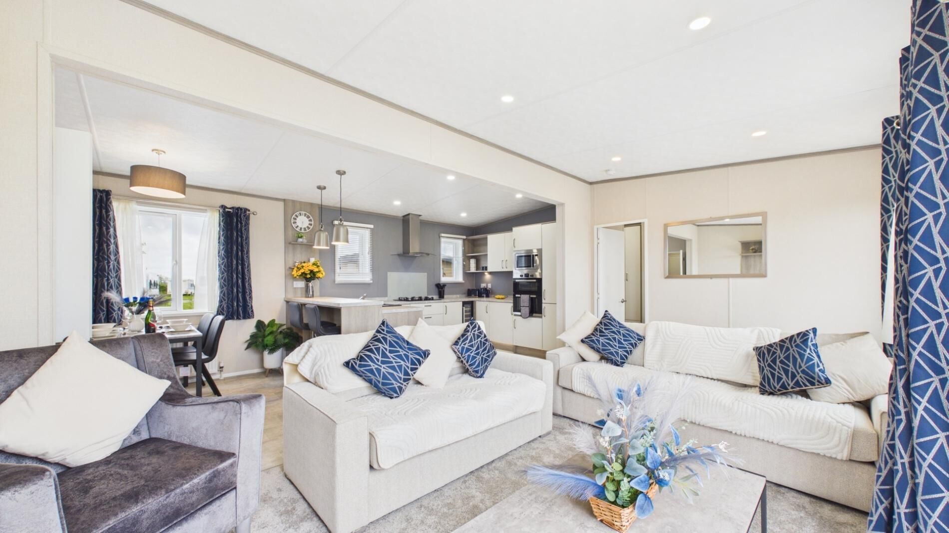 A modern living room with a sofa, armchair, and a dining area with a table and chairs.