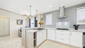 Een moderne keuken met een centraal eiland, inbouwmeubels, een gasfornuis en hanglampen.