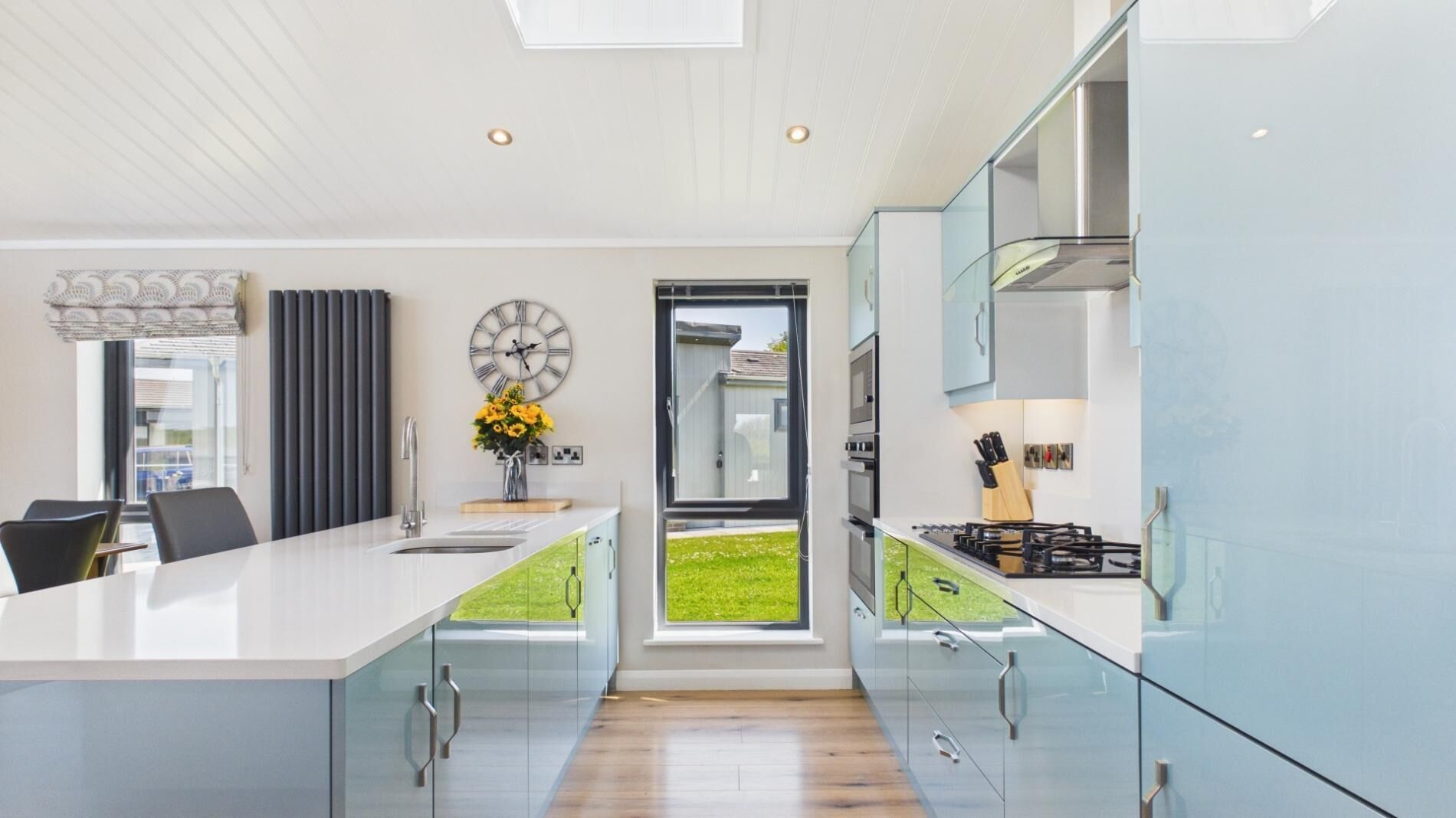 A modern kitchen with a large island, a dining area with chairs, a clock, and a view through a door.