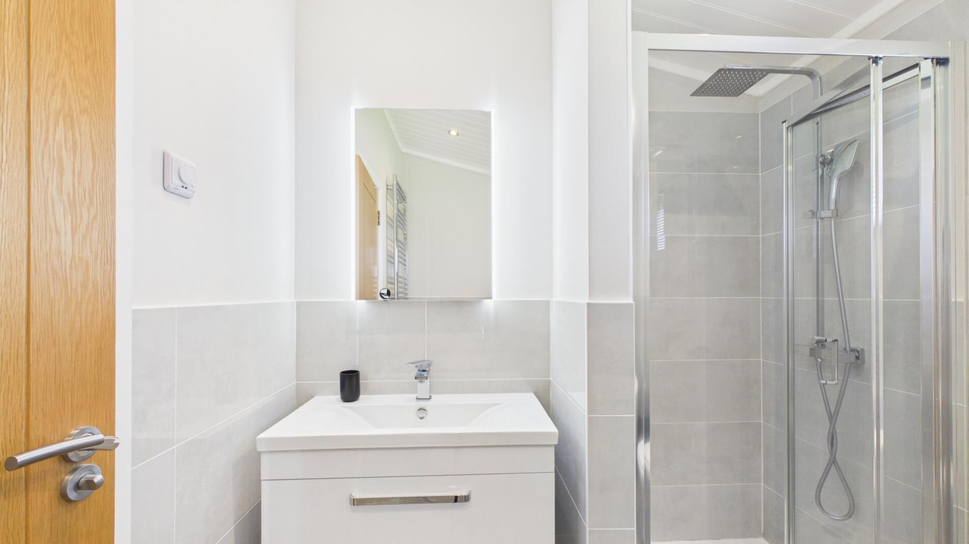 A modern bathroom with a white vanity, a mirror, and a glass-enclosed shower.