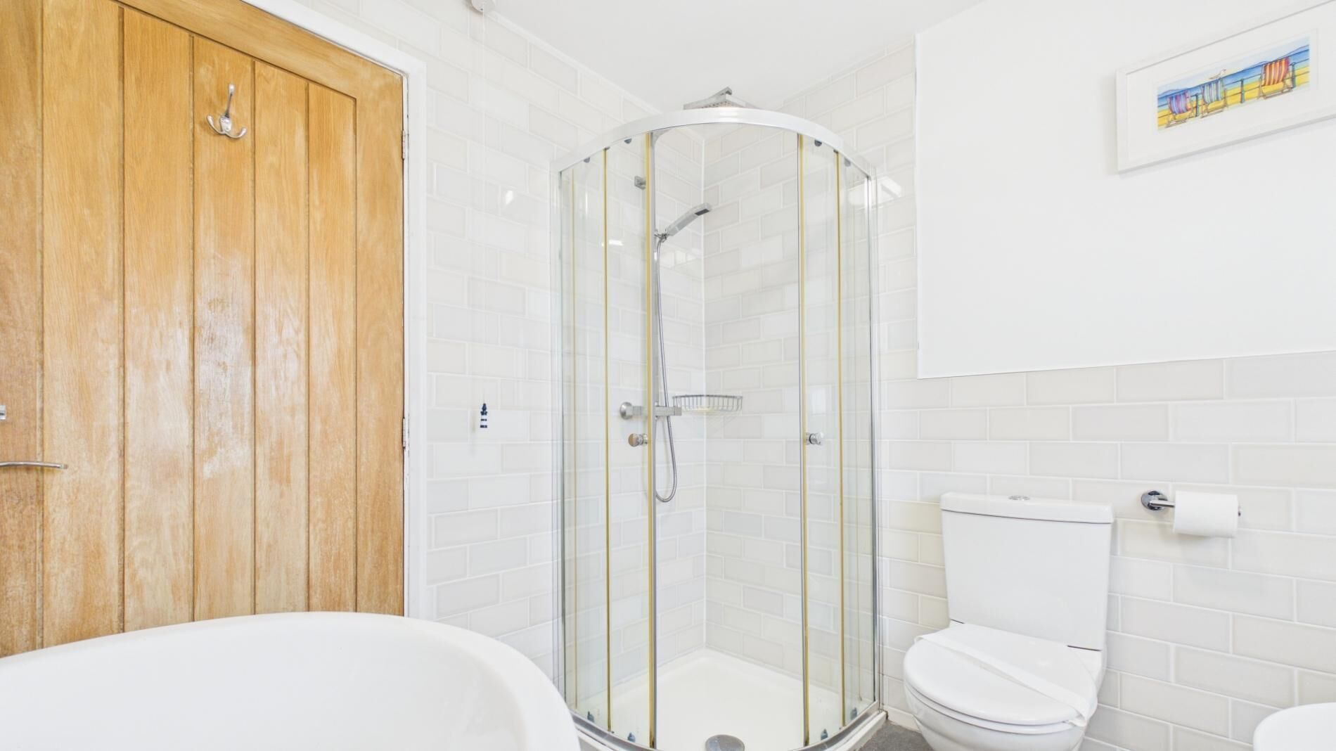 A bathroom with a wooden door, a glass shower enclosure, a white toilet, and a bathtub.
