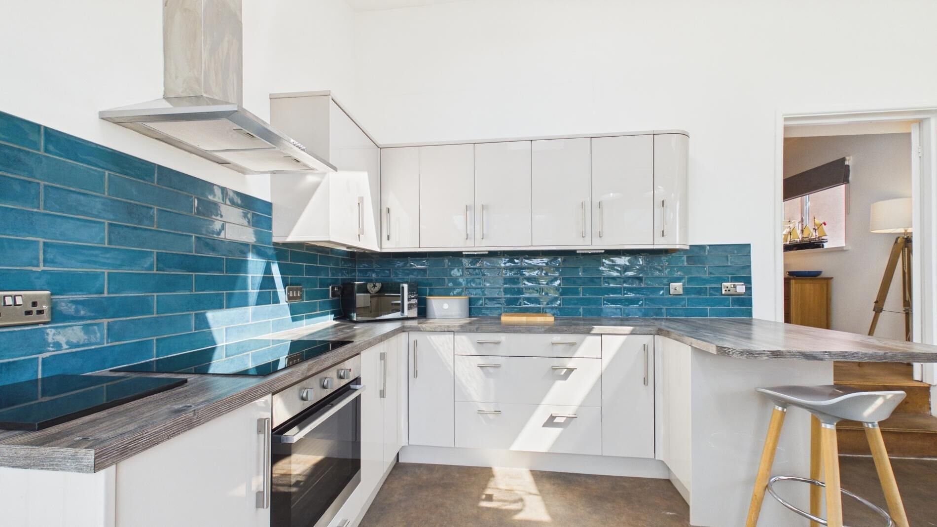 A modern kitchen with white cabinets, blue backsplash, and a built-in oven.