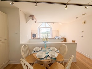 Un coin repas avec une table dressée pour quatre personnes, une vue sur la cuisine et une fenêtre donnant sur un paysage.