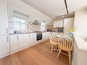 A modern kitchen with white cabinets, a wooden dining table, and a view of the outside.