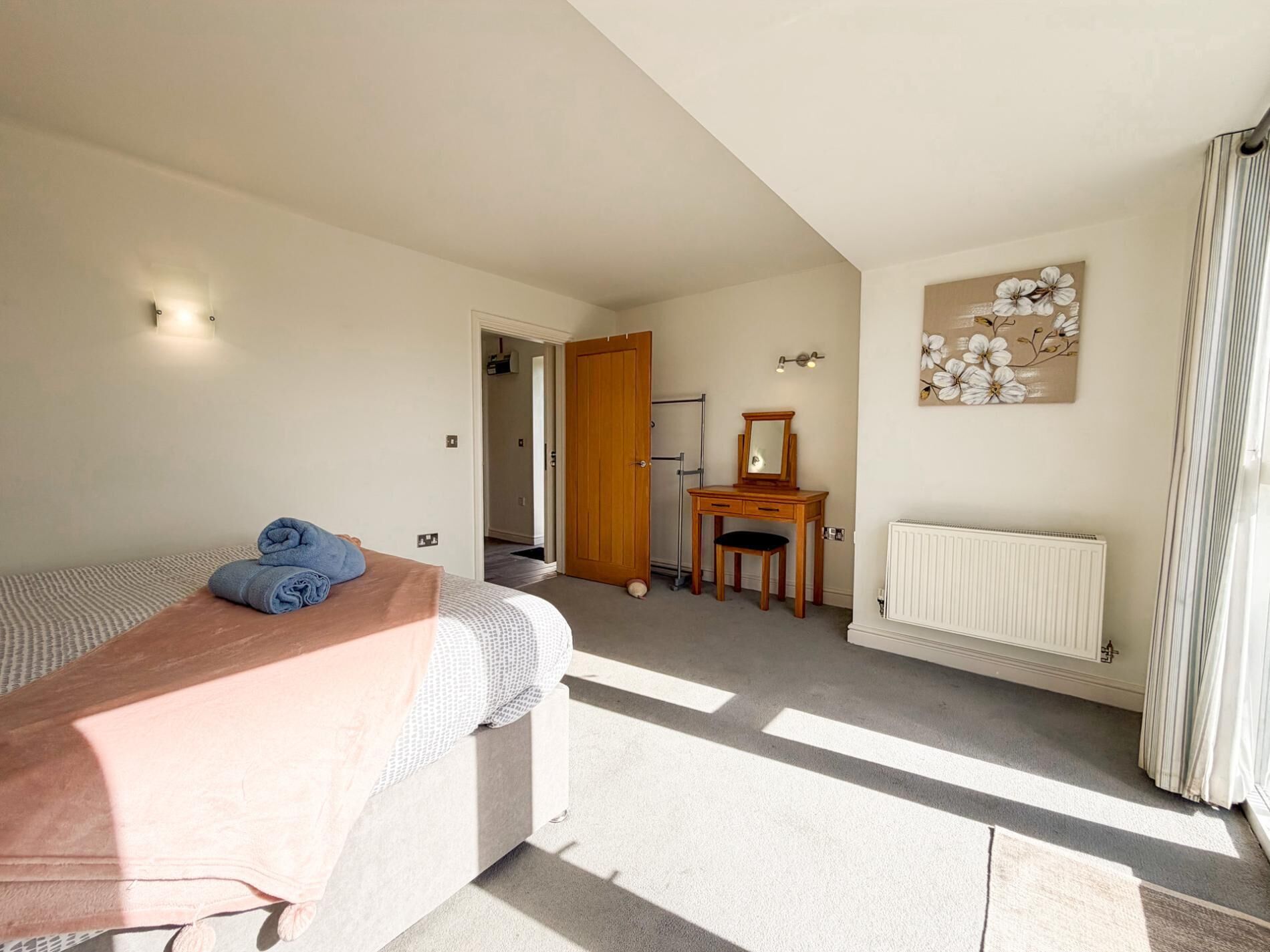 A bedroom with a bed, a desk, a radiator, and a door leading to another room.