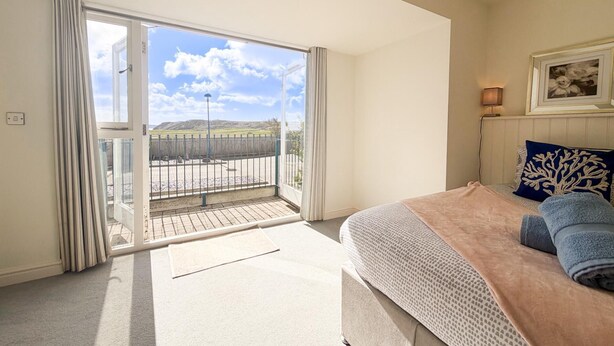 Un dormitorio con cama, ventana con cortinas, vista al exterior y lámpara en la mesita de noche.