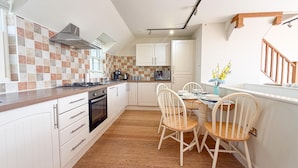 Una cocina con gabinetes blancos, salpicadero de azulejos, encimera de madera y un comedor con mesa y sillas.