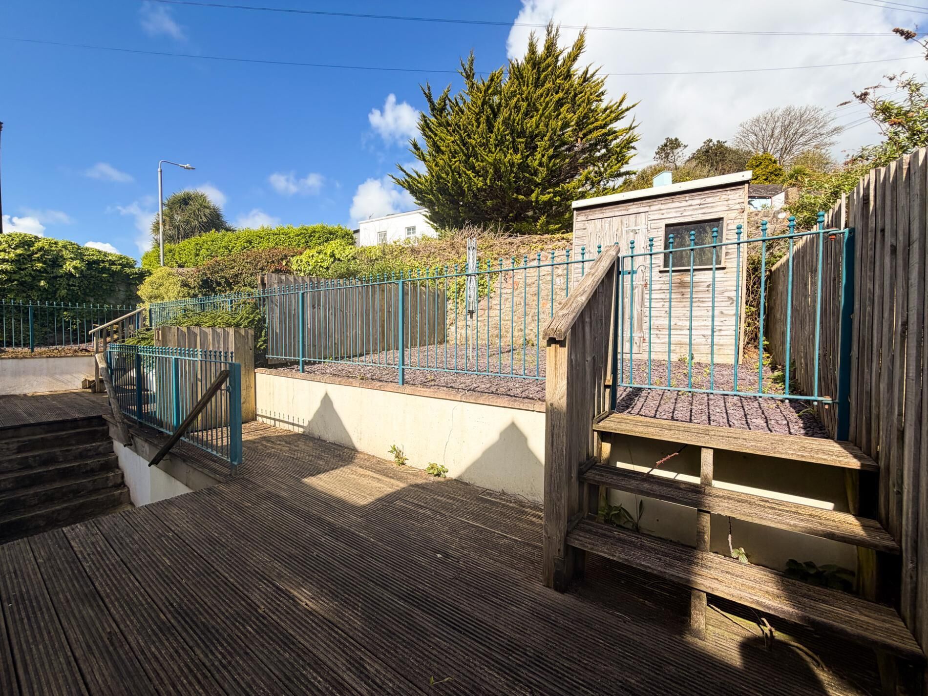 A wooden deck with a metal railing, a staircase, and a small building with a window.