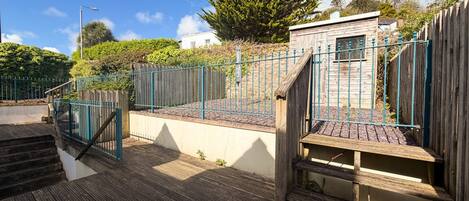 A wooden deck with a metal railing, a staircase, and a small building with a window.