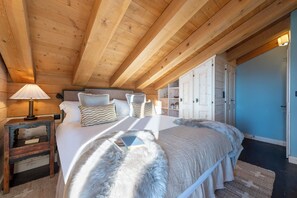 Eine Holzbalkendecke, ein Bett mit einer flauschigen weißen Decke, ein Nachttisch und eine Lampe.