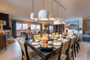 Ein Essbereich mit einem Holztisch, gedeckt für das Frühstück, einer Küche im Hintergrund und Blick ins Freie durch große Fenster.