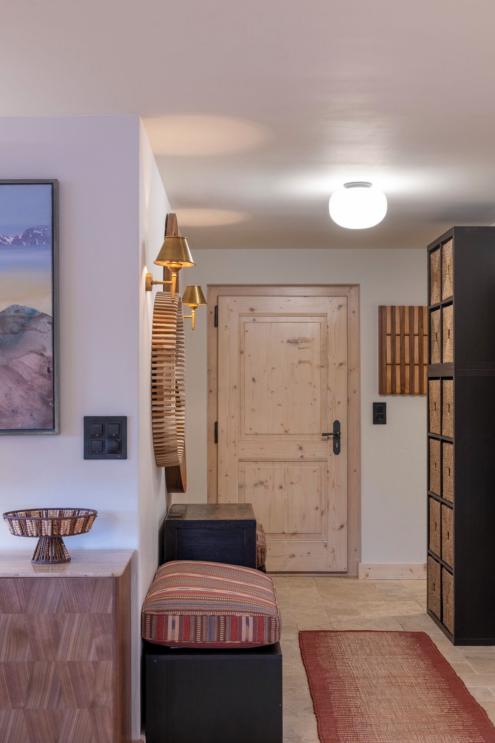 Een kamer met een houten deur, een wandlamp, een rieten mand en een gestreept kussen.